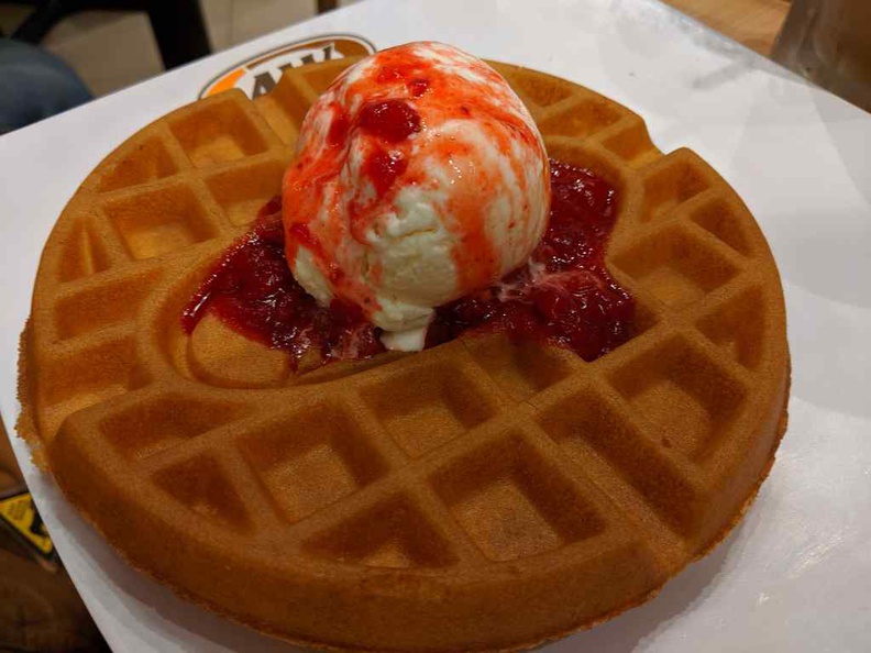 Strawberry waffles dessert, with berry bits and sauce sprinkled over a vanilla ice cream scoop