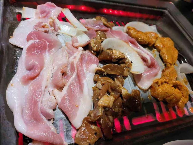 A hearty grill of bacon and chicken simmering on an electric grill at Kim Korean BBQ Shabu Shabu