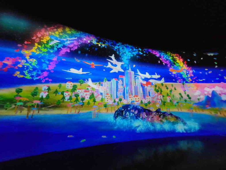 An animated city with scanned flying planes and a giant rainbow whale taking center stage